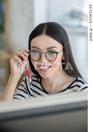 Dark-haired pretty woman in eyeglasses smiling nicely while watching something 65063149
