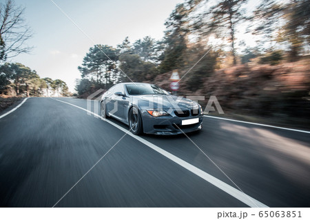 Grey business class sedan on the forest highway across oak trees Grey business class sedan on the forest highway across oak trees 65063851