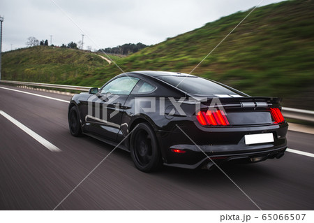 Black sedan with white stripes on it on the green landscapes, back view 65066507