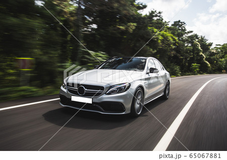 Silver business class sedan racing in the rain forest in the dusk time Silver business class sedan racing in the rain forest in the dusk time 65067881