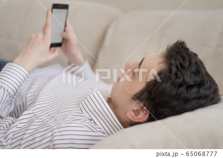 Teenager young man lying on sofa at home, holding Teenager young man lying on sofa at home, holding 65068777