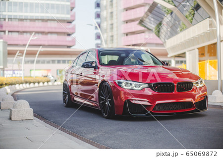 Red universal sedan touring in the city streets, across modern buildings 65069872