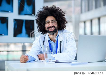 Portrait of cheerful male doctor sitting in hospital, looking at camera. 65071144