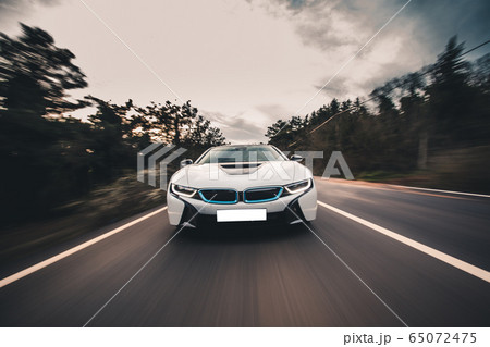 White sport car high speed drive in the forest across green trees, front view 65072475
