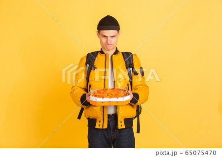 Contacless delivery service during quarantine. Man delivers food and shopping bags during insulation. Emotions of deliveryman isolated on yellow background. 65075470