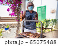 elderly lady cooking on a barbecue with face mask 65075488
