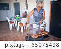 happy elderly lady cooking on a barbecue together with her family 65075498