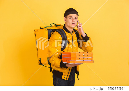 Contacless delivery service during quarantine. Man delivers food and shopping bags during insulation. Emotions of deliveryman isolated on yellow background. Contacless delivery service during quarantine. Man delivers food and shopping bags during insulation. Emotions of deliveryman isolated on yellow background. 65075544
