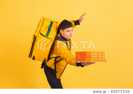 Contacless delivery service during quarantine. Man delivers food and shopping bags during insulation. Emotions of deliveryman isolated on yellow background. Contacless delivery service during quarantine. Man delivers food and shopping bags during insulation. Emotions of deliveryman isolated on yellow background. 65075550