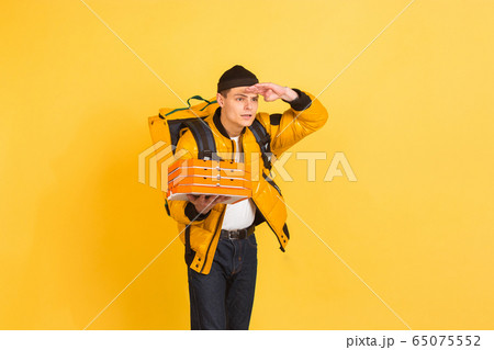 Contacless delivery service during quarantine. Man delivers food and shopping bags during insulation. Emotions of deliveryman isolated on yellow background. Contacless delivery service during quarantine. Man delivers food and shopping bags during insulation. Emotions of deliveryman isolated on yellow background. 65075552