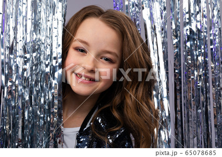 European beautiful teenage girl in a stylish outfit on a holiday peeks out from behind a tinsel European beautiful teenage girl in a stylish outfit on a holiday peeks out from behind a tinsel 65078685