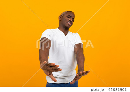 handsome smiling african man in a white t-shirt waving his hands in denial on an orange background handsome smiling african man in a white t-shirt waving his hands in denial on an orange background 65081901