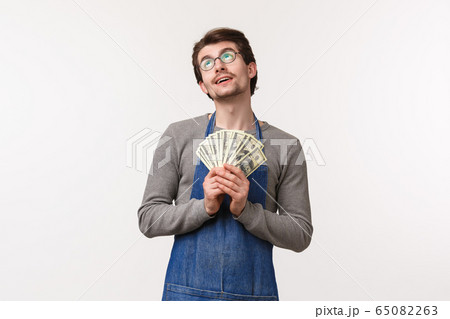 Small business, finance and career concept. Portrait of dreamy delighted handsome man in apron, employee receive his paycheck, holding earned money and dreaming of vacation, white background 65082263