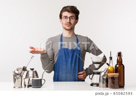 Barista, cafe worker and bartender concept. Portrait of confused and judgemental young man in apron, shurgging raise hand in dismay look skeptical, complain customer bad taste in coffee 65082593