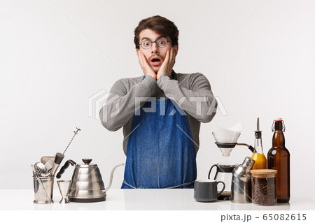 Barista, cafe worker and bartender concept. Shocked speechless young caucasian guy in apron, staring shocked look how customer drink his coffee wrong, standing near bar counter with chemex 65082615
