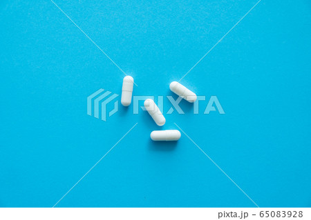 White pills on blue background. Medicine, medication, painkillers, tablet, medicaments, drugs, antibiotic, vitamin, treatment. Pharmacy theme. Top view on the pills scattered on the blue surface. 65083928