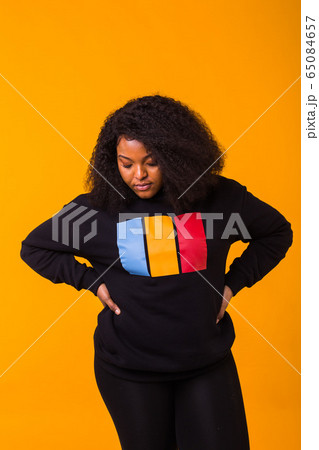 Beautiful African American woman having fun in black sweatshirt on a yellow background. Street fashion photo with afro hairstyle. Beautiful African American woman having fun in black sweatshirt on a yellow background. Street fashion photo with afro hairstyle. 65084657