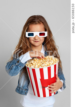 child girl wearing red-blue 3d glasses having fun and holding popcorn bucket child girl wearing red-blue 3d glasses having fun and holding popcorn bucket 65086150