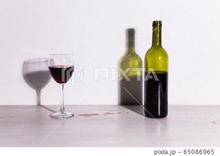 Bottle with wine and glass, red puddle of wine on the table. Cleaning after party concept. 65086965