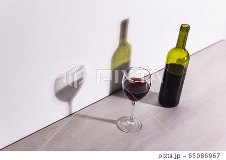 A glass of wine and a bottle casts a long shadow from the evening sun. A glass of wine and a bottle casts a long shadow from the evening sun. 65086967