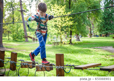Happy kid playing at adventure park, holding ropes Happy kid playing at adventure park, holding ropes 65088901