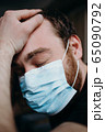 Sad balding adult man in a medical mask holding his head with his hands. 65090792