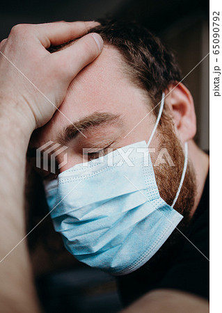 Sad balding adult man in a medical mask holding his head with his hands. 65090792