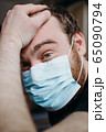 Sad balding adult man in a medical mask holding his head with his hands. 65090794