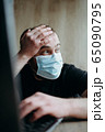 Coronavirus, an adult male with a beard works at a laptop. Protective respiratory mask. 65090795