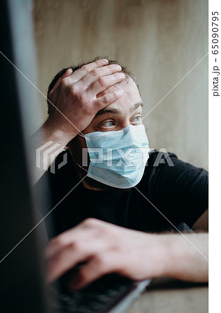 Coronavirus, an adult male with a beard works at a laptop. Protective respiratory mask. Coronavirus, an adult male with a beard works at a laptop. Protective respiratory mask. 65090795