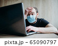 Coronavirus, an adult male with a beard works at a laptop. Protective respiratory mask. 65090797