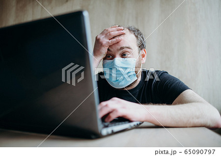 Coronavirus, an adult male with a beard works at a laptop. Protective respiratory mask. 65090797