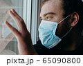 Coronavirus. Sick man of corona virus looking through the window and wearing mask protection. 65090800