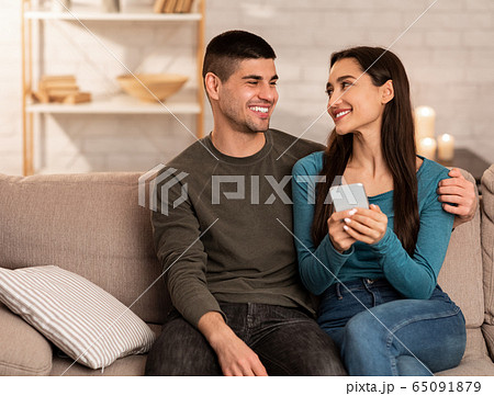 Couple using cell phone sitting on couch, free space Couple using cell phone sitting on couch, free space 65091879