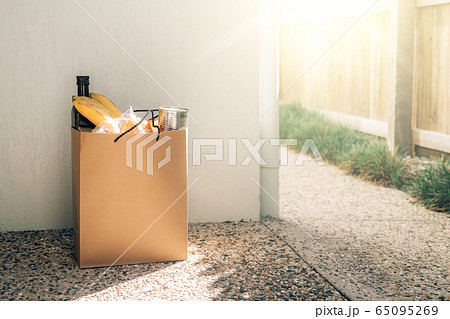 Paper bag with food on the floor next to the wall of house. 65095269