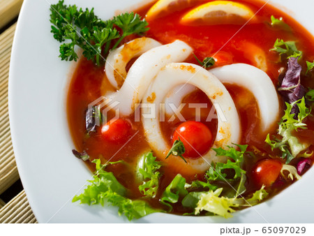 Spicy tomato soup with sea squids and greens served in a white bowl 65097029