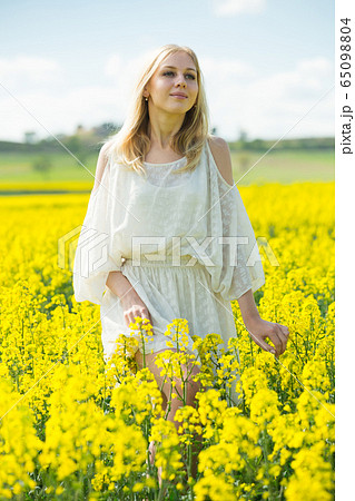 Girl posing in rape seed flowers field posing in white dress at sunny day 65098804