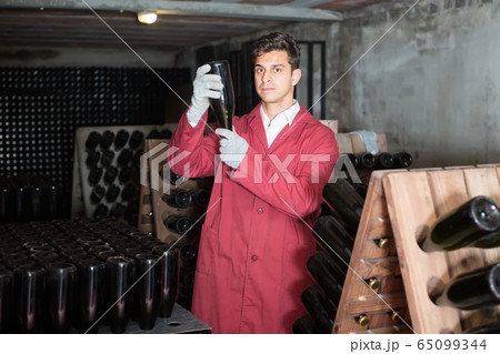 cheerful man wearing uniform working with bottle storage racks cheerful man wearing uniform working with bottle storage racks 65099344