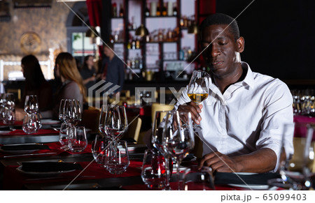 African-american man with glass of white wine is expecting woman in a luxury restaurant African-american man with glass of white wine is expecting woman in a luxury restaurant 65099403