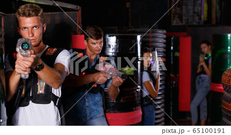 Young guy holding colored laser guns and took aim during laser tag game in labyrinth Young guy holding colored laser guns and took aim during laser tag game in labyrinth 65100191
