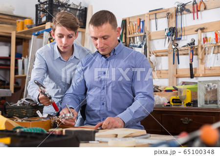 father and teen son working with wood plank in workshop 65100348