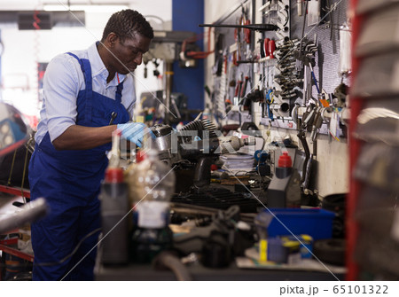 Afro american worker in overalls inspects a motorcycle engine 65101322