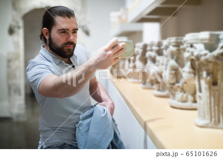 Adult male visitor using phone in sculptures exposition at museum Adult male visitor using phone in sculptures exposition at museum 65101626