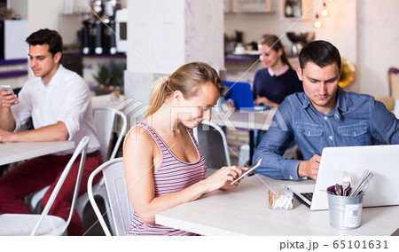 Young smiling woman with boyfriend busying with device in modern cafe Young smiling woman with boyfriend busying with device in modern cafe 65101631