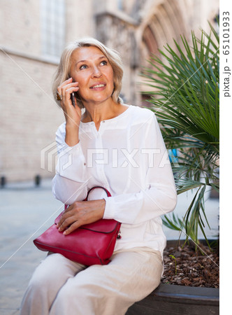 Mature positive female talking on phone in the historical city center 65101933