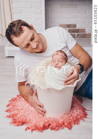 ther hugs the baby. a newborn baby, wrapped in a blanket, sleeps in a basket against the background of the fireplace. concept of childhood, health care, IVF, family home ther hugs the baby. a newborn baby, wrapped in a blanket, sleeps in a basket against the background of the fireplace. concept of childhood, health care, IVF, family home 65103625