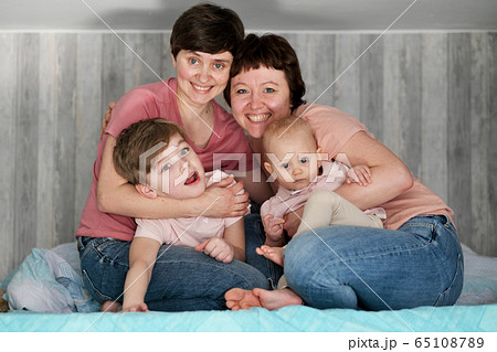 A young homosexual lesbian couple with two children at home, on the bed. 65108789