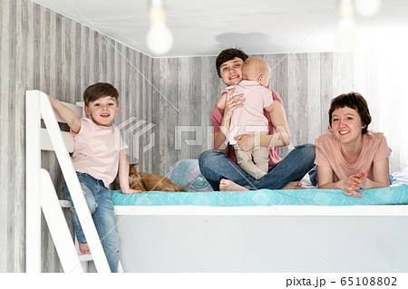 A young homosexual lesbian couple with two children at home, on the bed. A young homosexual lesbian couple with two children at home, on the bed. 65108802