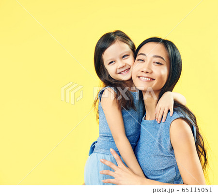 Happy mother and her child daughter hugging on yellow background. 65115051