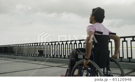 Young man disabled in wheelchair rides along the promenade 65120946